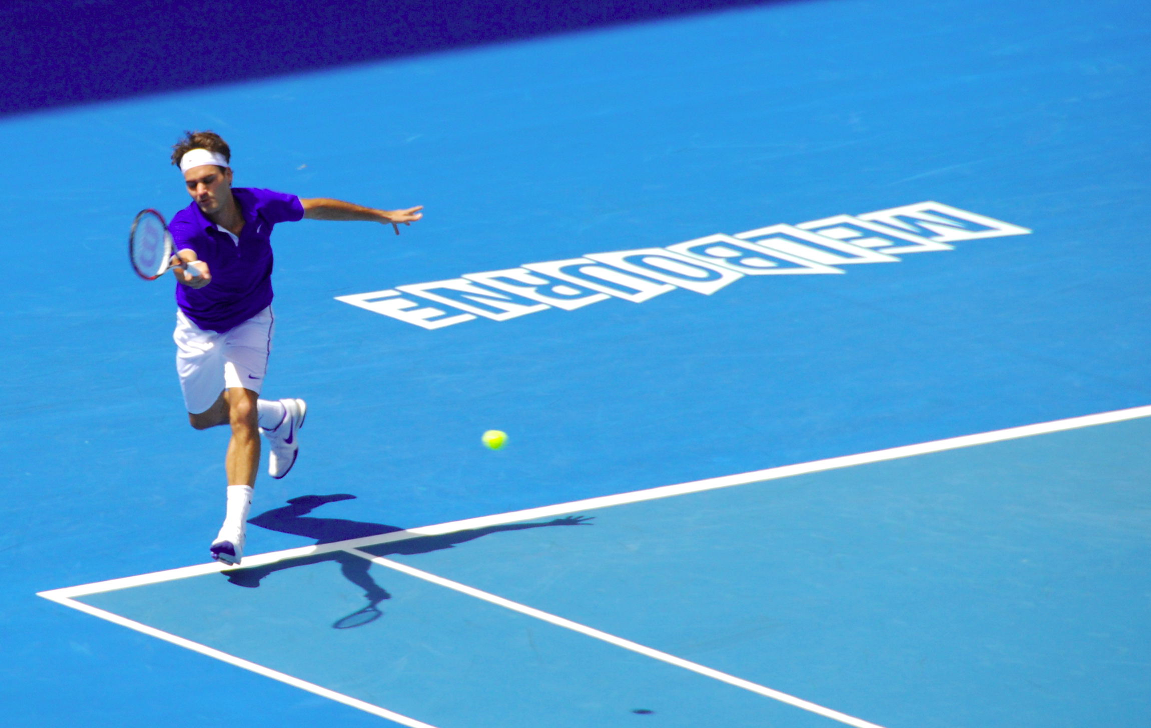 Ein Tennisspielen mit Schläger in der Hand rennt auf blauem Boden