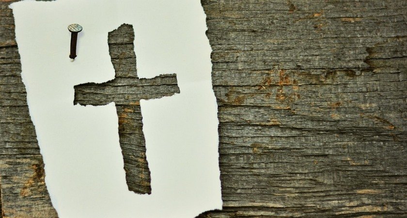 Kreuz in Papier gestanzt mit Nagel an der Wand