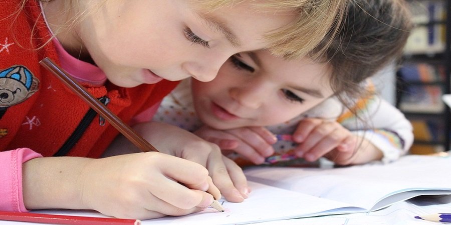 Lernende Person mit Stift in der Hand, einer Tasse und einem Tablet am Tisch und 2 Notizblöcken.