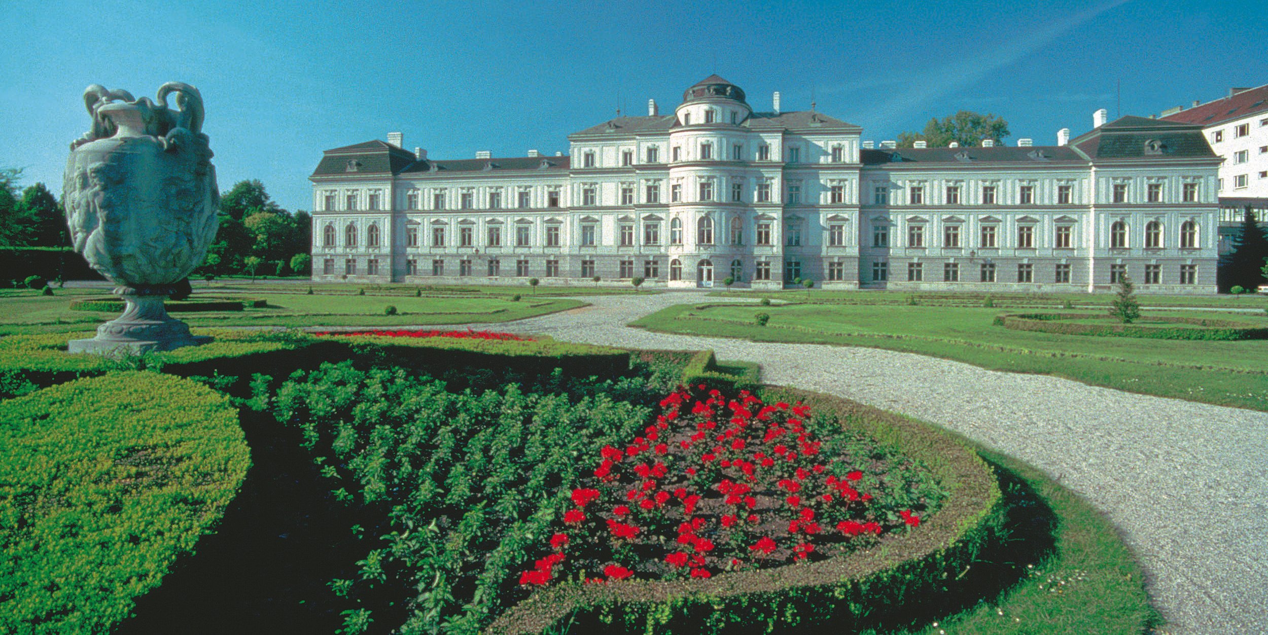 Palais Augarten in wien mit grüner saftiger Wiese im Vordergrund und rotem Blumenbeet