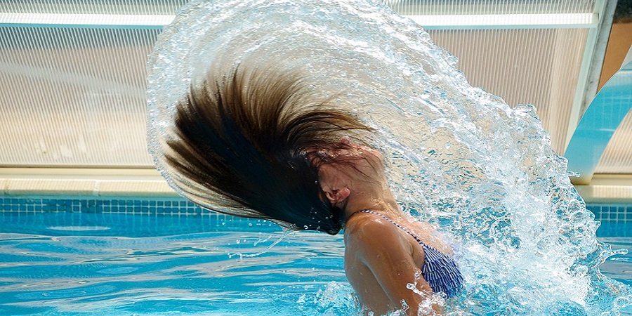 Frau die aus dem Wasser auftaucht und ihre Haare über sich wirft.