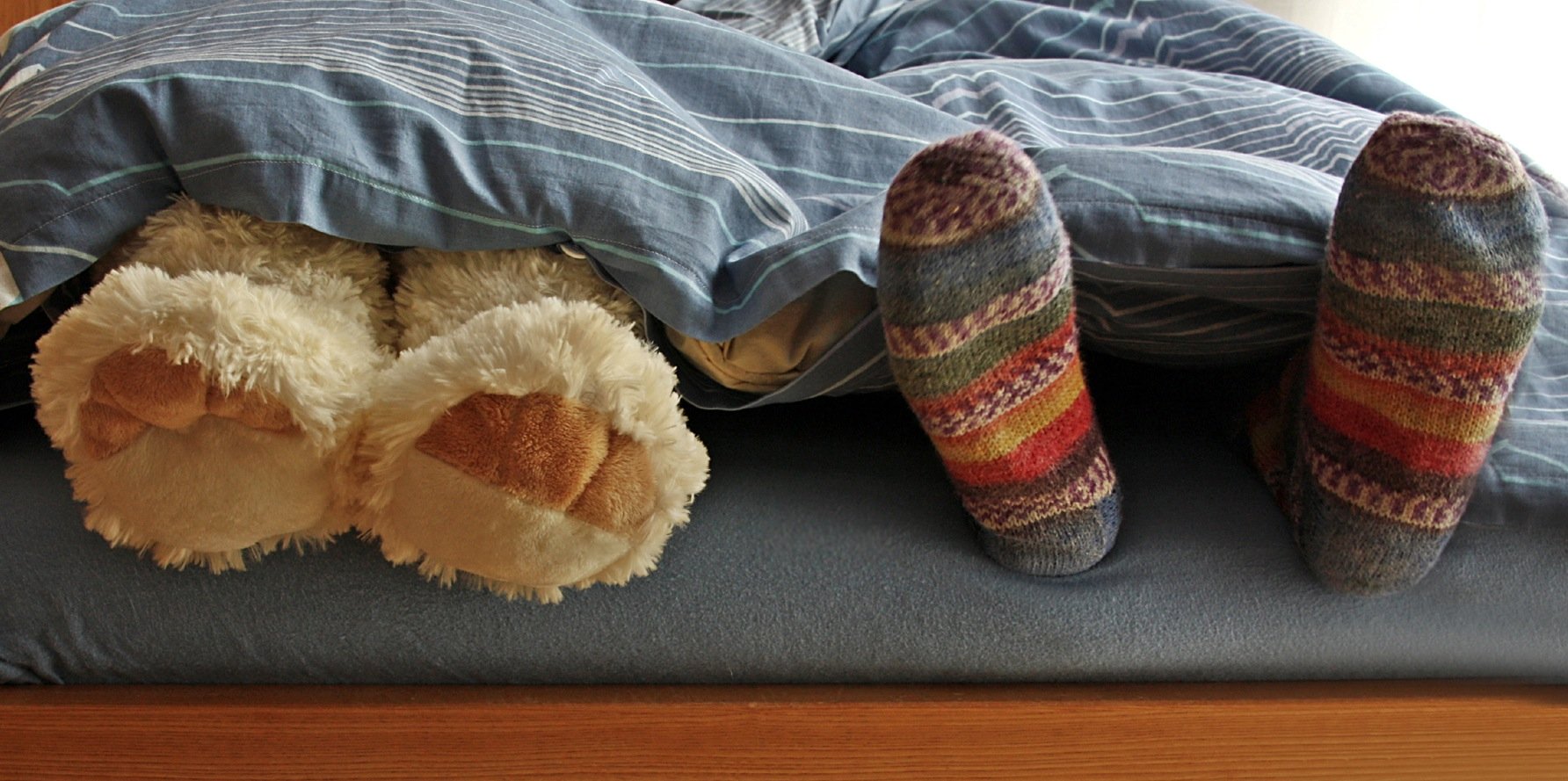Füße einer Person und eines Teddybärs, die unter einer Decke hervorlugen