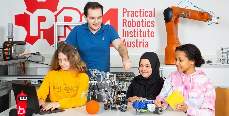 Ein Mann erklärt drei jungen Mädchen, wie sie einen Roboter zusammenbauen können