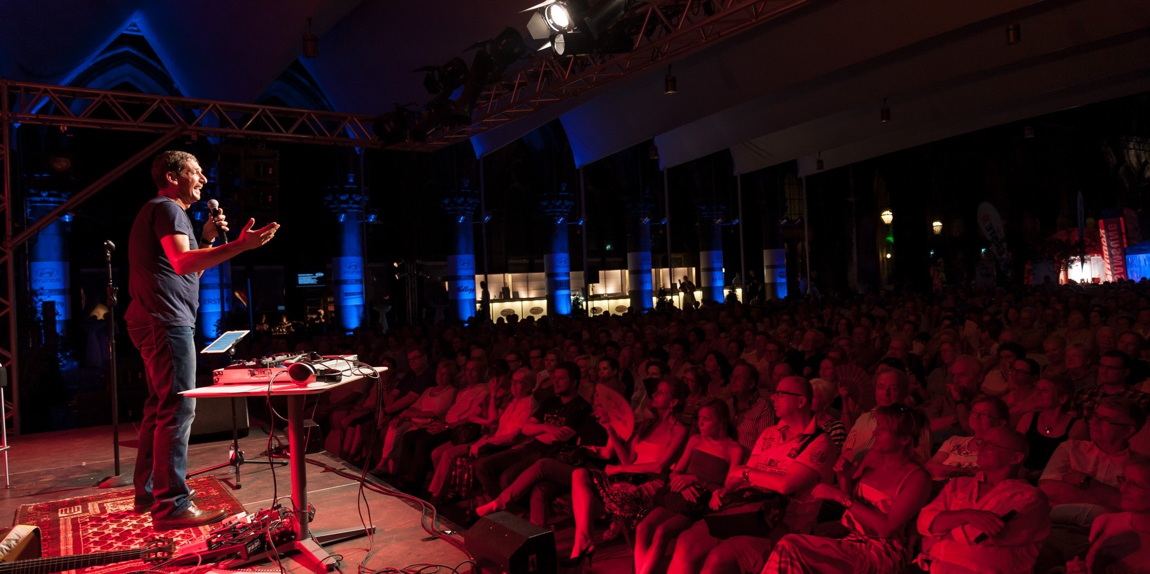Kabarettist Gernot Krulis vor Publikum auf der Bühne im Rotlicht