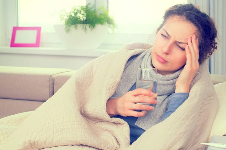 Frau liegt auf Couch mit Glas Wasser in der Hand und ist krank wegen Biowetter