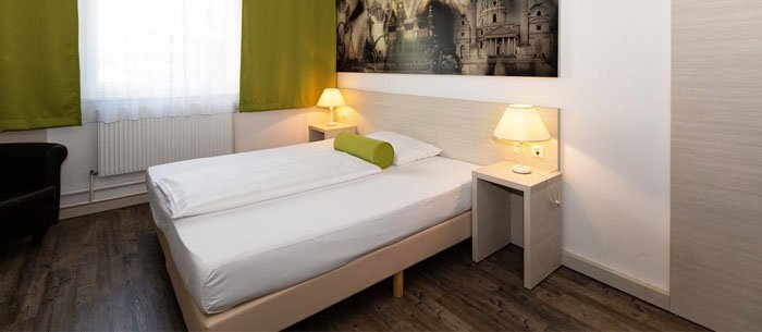 Zu sehen ist das ein Zimmer im Lifehotel Vienna Airport. Der Einrichtungsstil ist schlicht und in den Farben grün, beige und weiß gehalten.