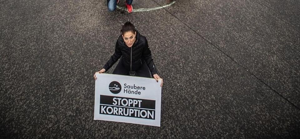 Antikorruptionsbegehren: Frau kniet mit Schild am Boden, Text lautet "Stoppt Korruption"
