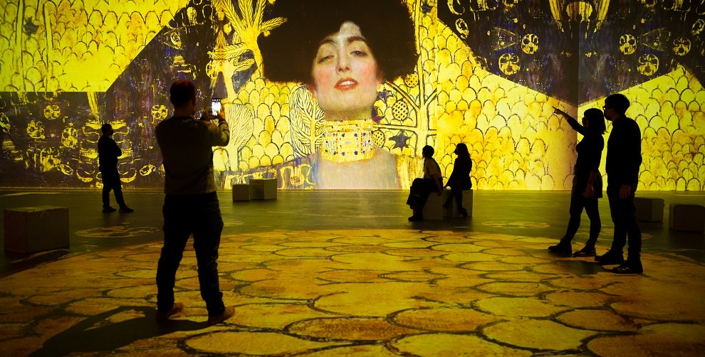 Aufnahme der Ausstellung Klimt Experience, Menschen bewegen sich inmitten übergroßer Projektionen der Klimt-Werke