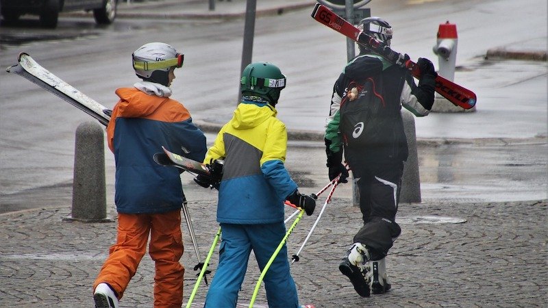Drei Skifahrer in der Stadt, mit Skiern über den Schultern.