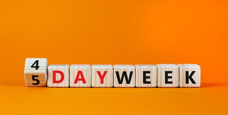 Bild mit orangem Hintergrund, davor Bauklötzchen mit Buchstaben und Zahlen drauf, die "4 Tage Woche" schreiben