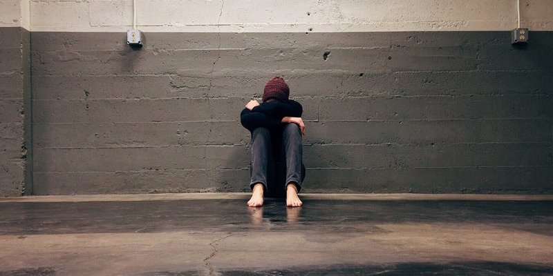 Angststörungen: Mann sitzt zusammengekauert an einer Wand und fürchtet sich