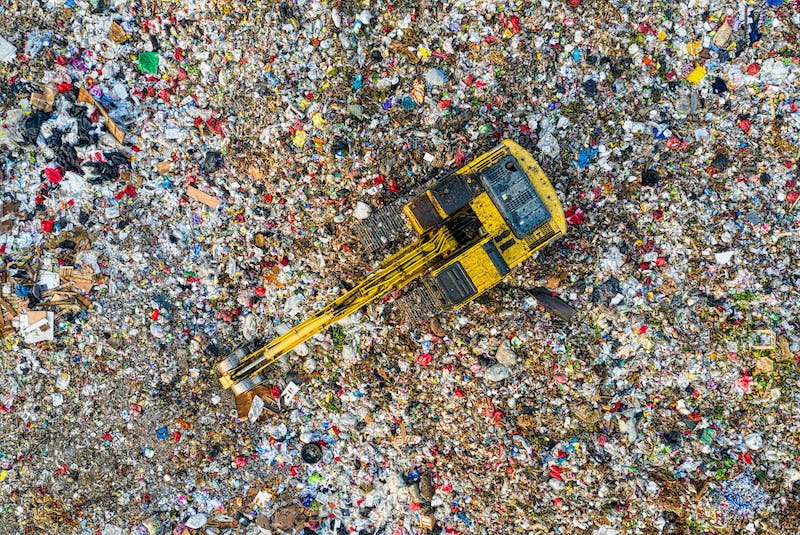 Gelber Bagger auf einem Müllberg aus der Vogelperspektive