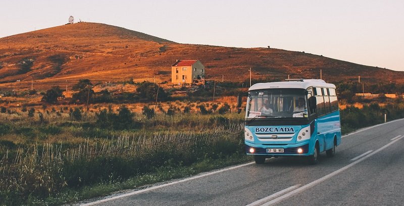 Das Bild zeigt einen kleinen Reisebus mit einem Hügel im Hintergrund.