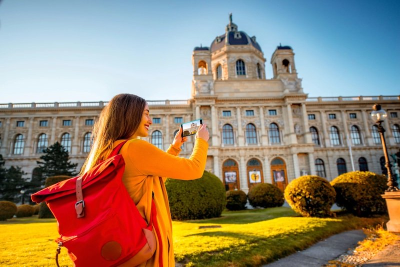 Junge Frau fotografiert mit dem Mobile das Kunsthistorische Museum in Wien von außen